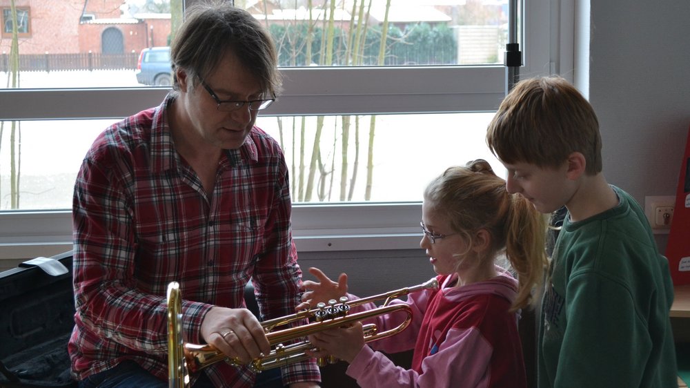 Ein Musiklehrer erklärt zwei Schülern eine Trompete.